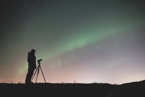 person standing near a tripod under green sky with stars